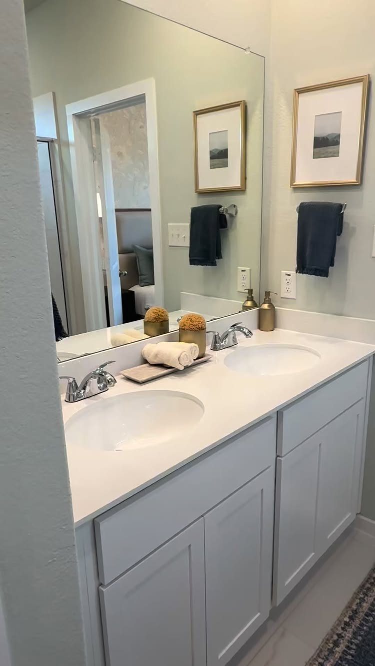 White bathroom vanity with two sinks, silver faucets, and a large wall mirror.