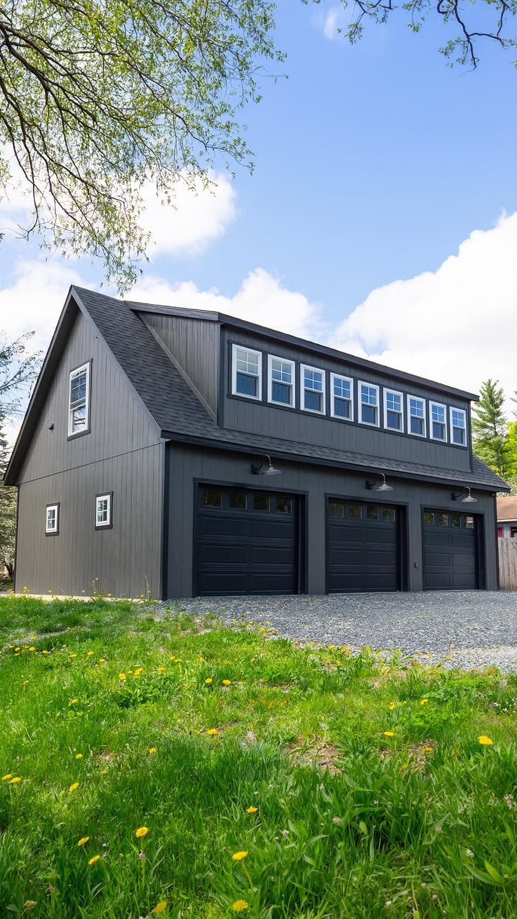 A dark gray two-story building with three garage doors and a long row of upper windows.