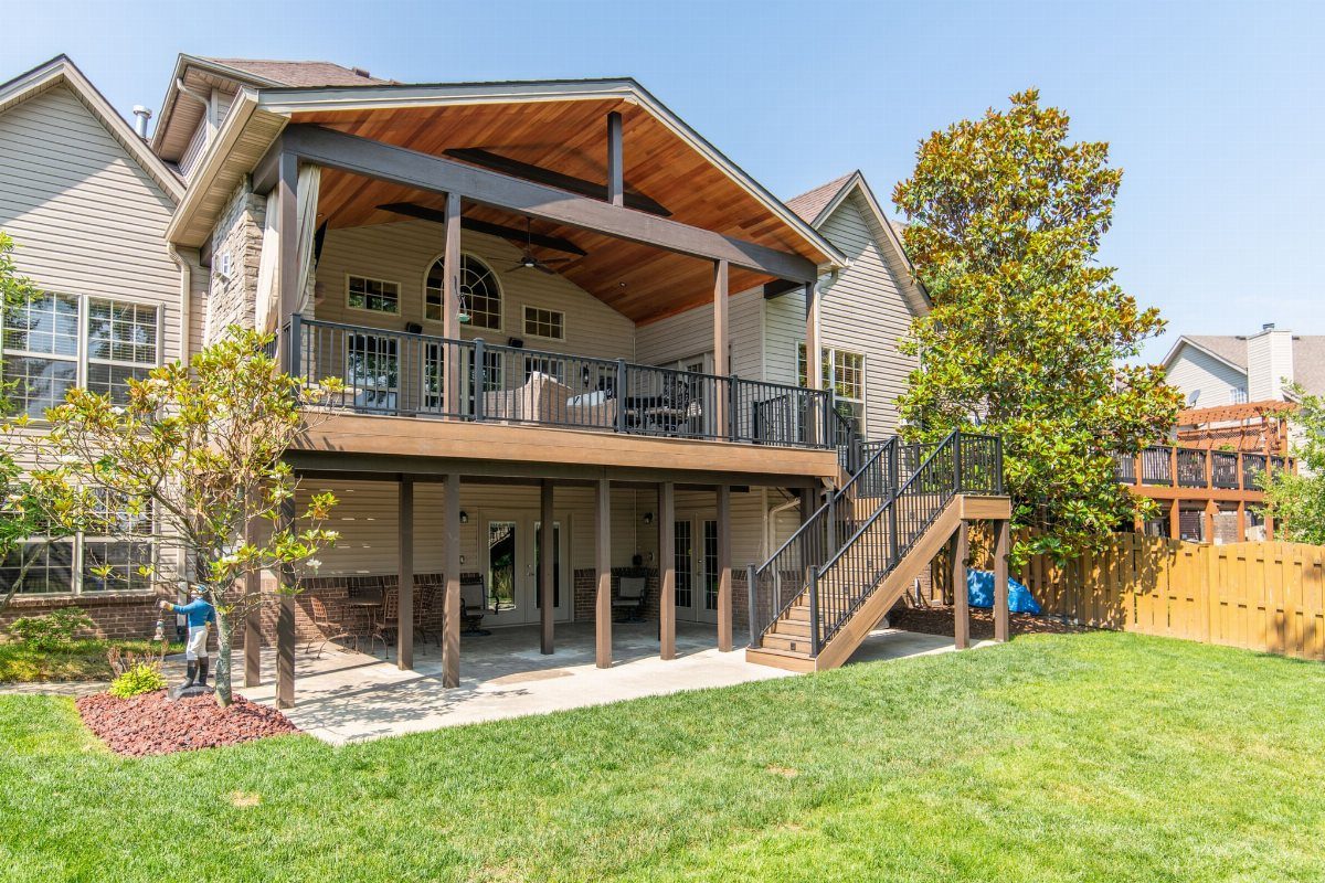 A large wooden two-story deck with a gable roof attached to a residential house.
