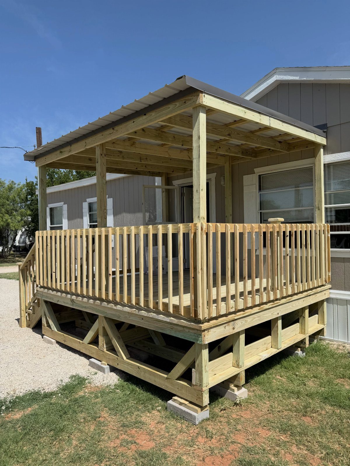 A wooden deck with a sloped metal roof and protective railings built next to a house.