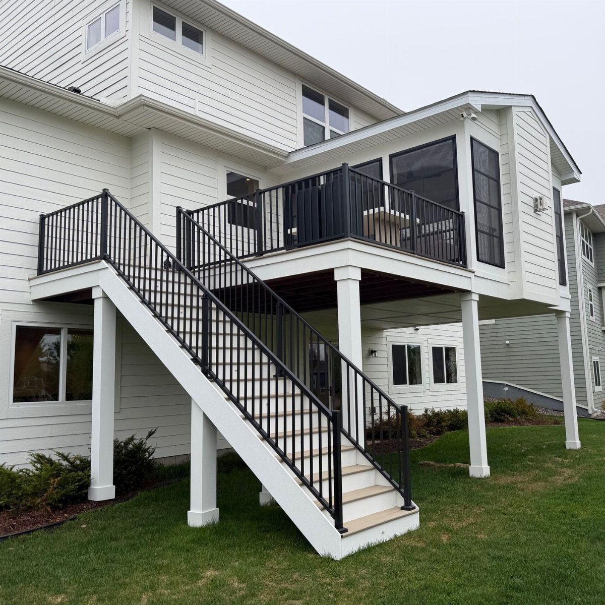 An elevated white wooden deck with black railings and stairs leading to a green lawn.