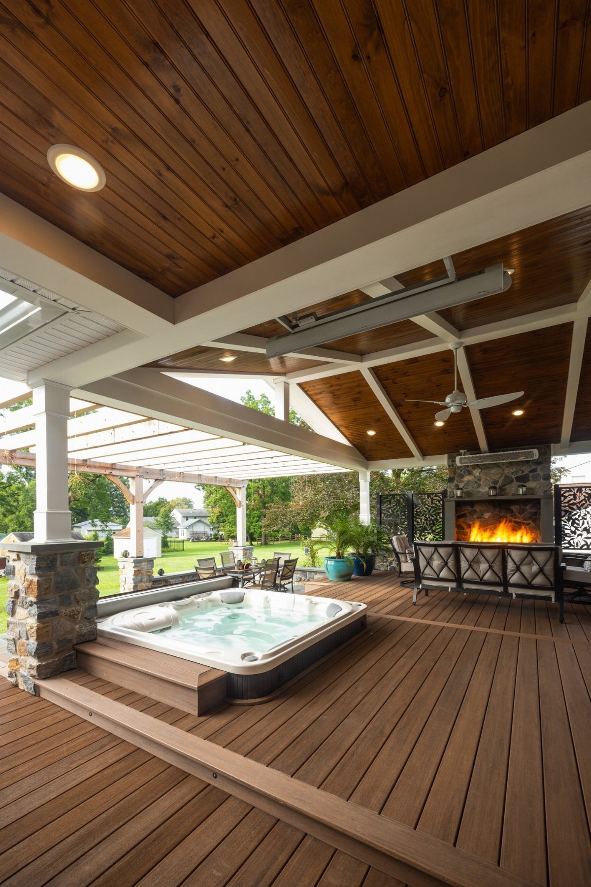 A luxury wooden deck with a hot tub, outdoor fireplace, and vaulted wood ceiling.