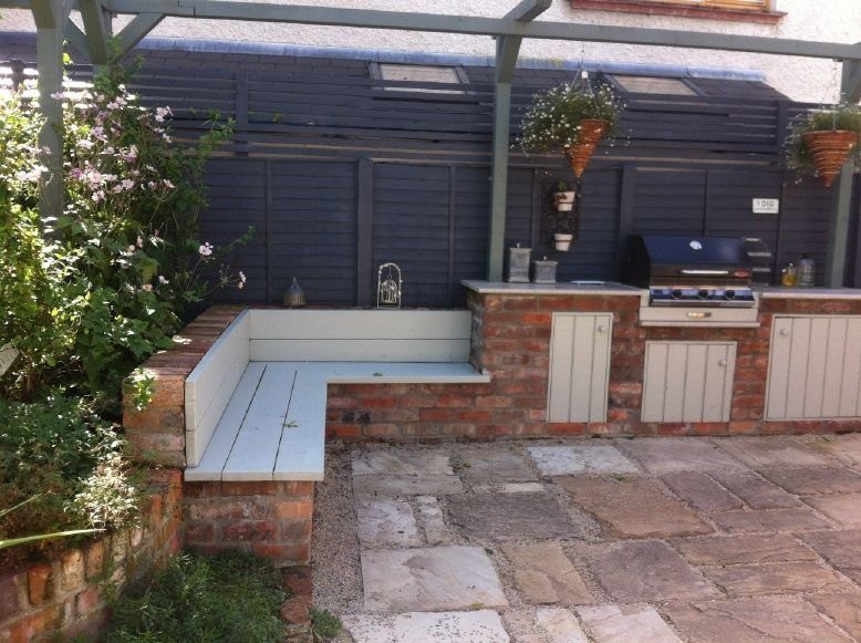 Built-in brick outdoor kitchen with a grill and integrated wooden bench seating on a stone patio.