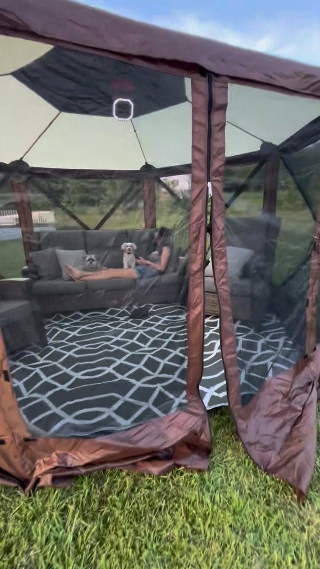 A brown mesh mosquito canopy tent containing a sofa and rug on a grassy lawn.