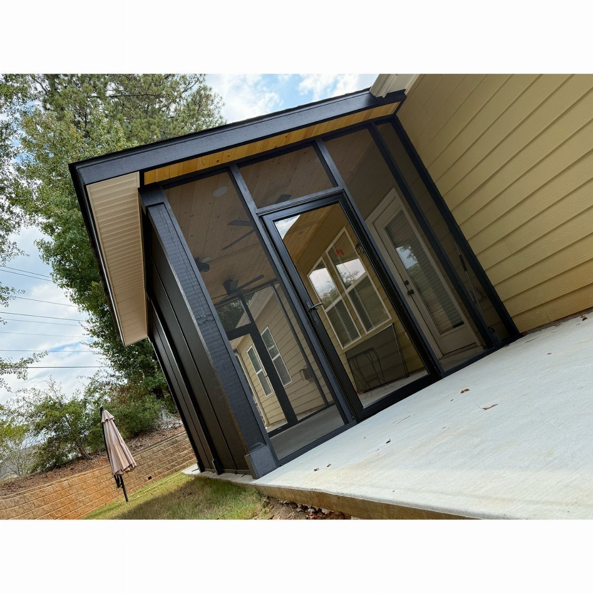 A black screened-in porch attached to a yellow house overlooking a green backyard.