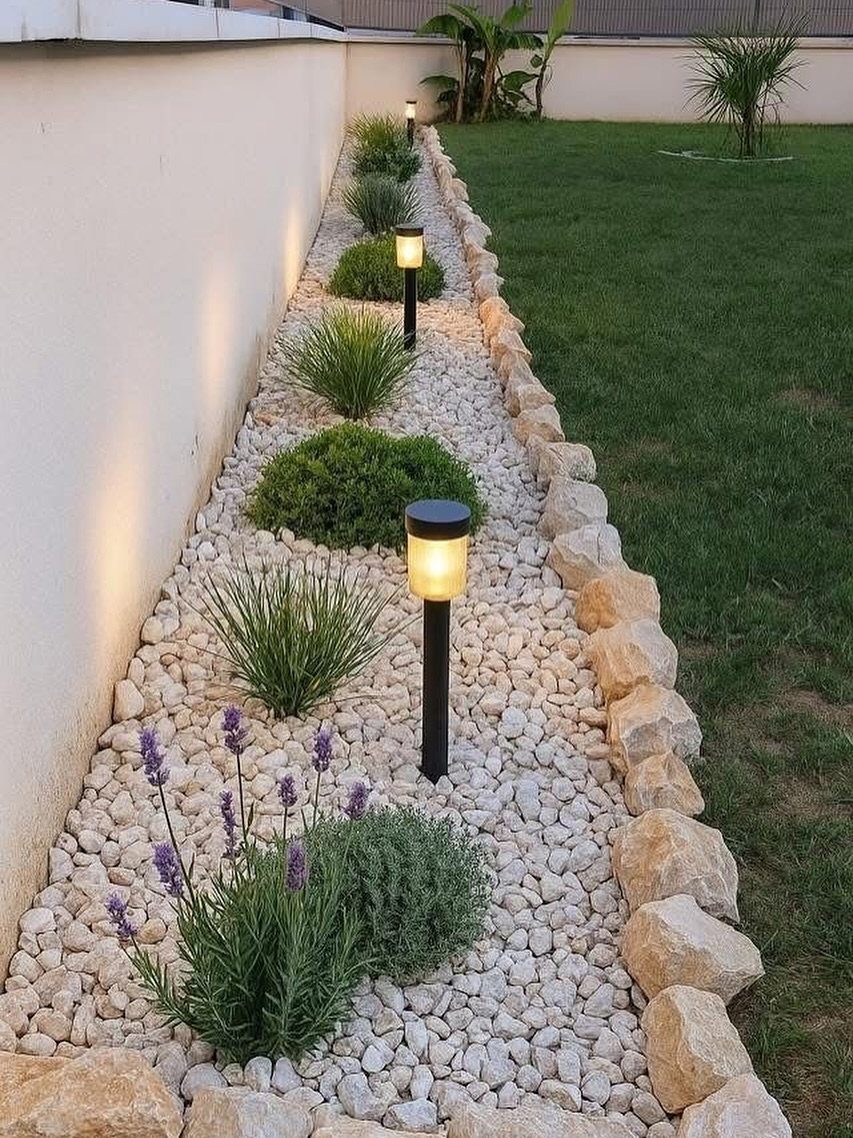 Decorative light stones and small plants line a white wall with solar pathway lights.