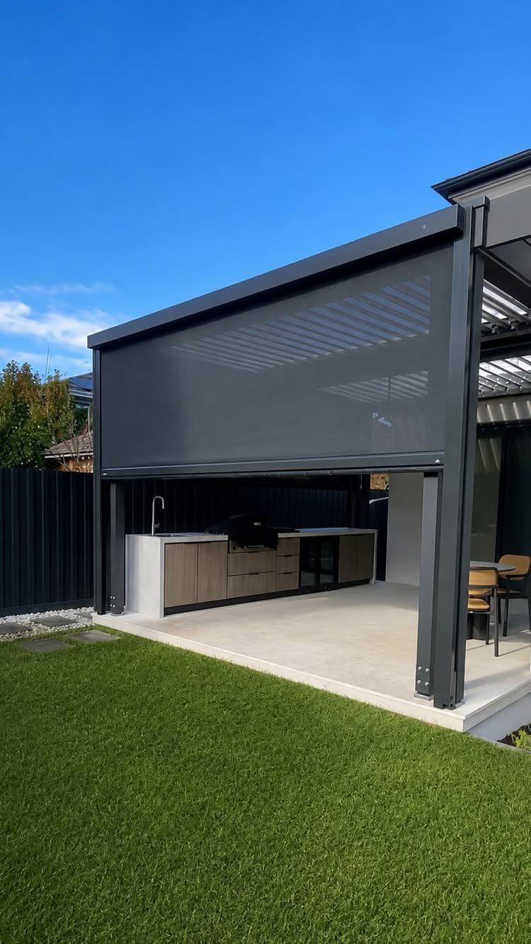 16 Backyard Patio Designs for Fire Pits, Pergolas & Outdoor Kitchens 3 Modern outdoor kitchen with built-in grill and sink under a dark grey pergola structure.