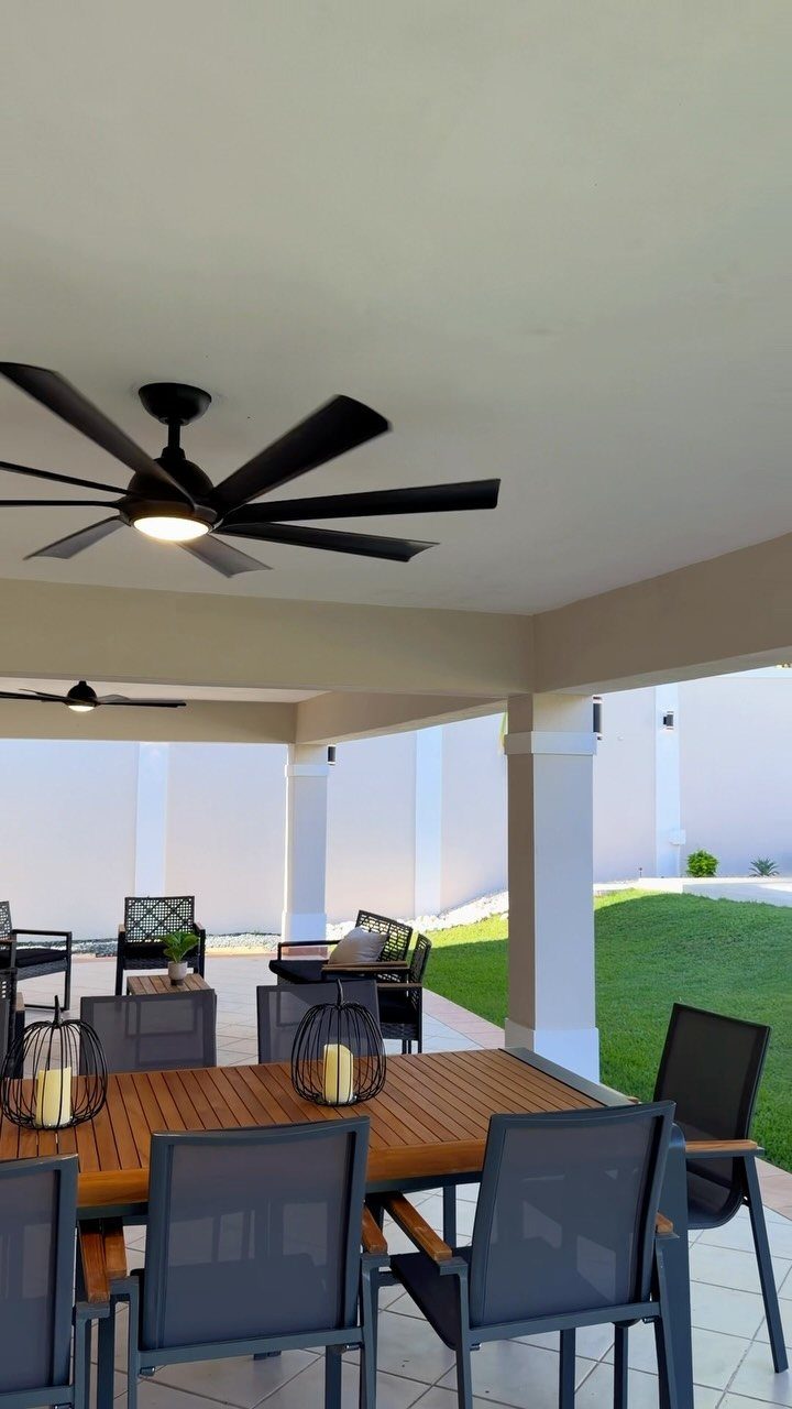 16 Backyard Patio Designs for Fire Pits, Pergolas & Outdoor Kitchens 9 Wooden dining table with dark grey chairs situated under a covered patio with a ceiling fan.