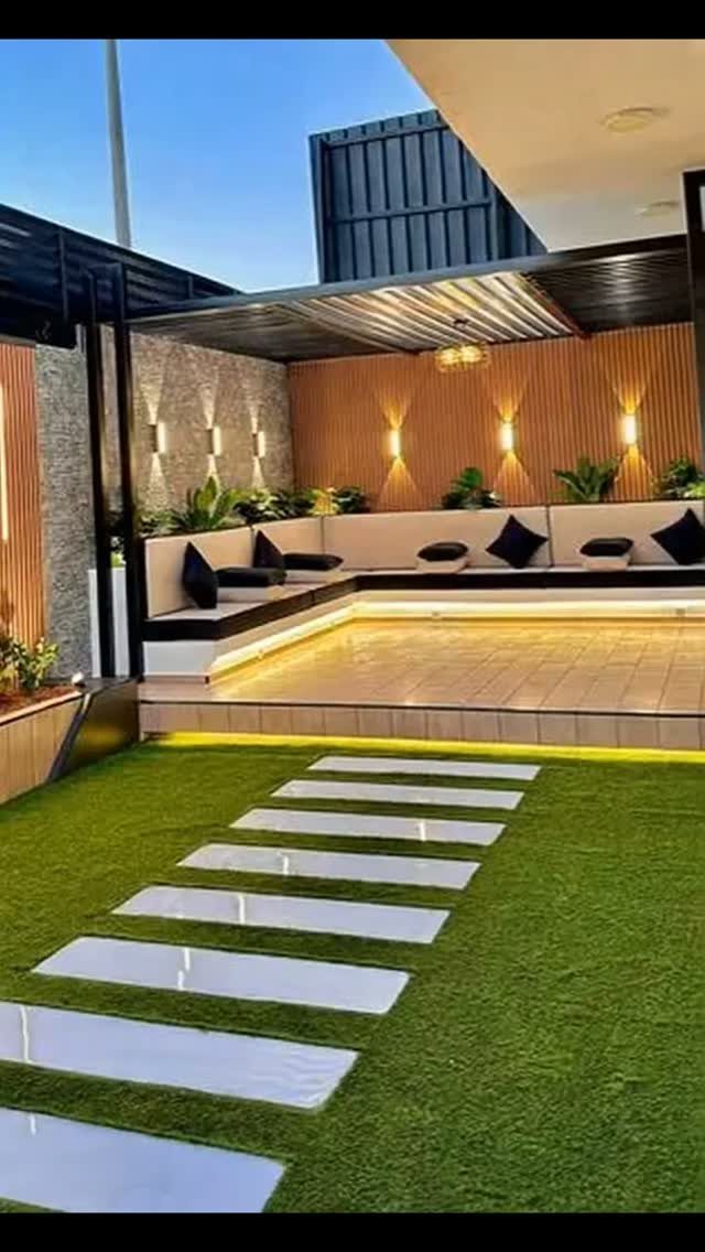 16 Backyard Patio Designs for Fire Pits, Pergolas & Outdoor Kitchens 11 Modern backyard patio with built-in seating, wooden accent walls, and stepping stones on green grass.
