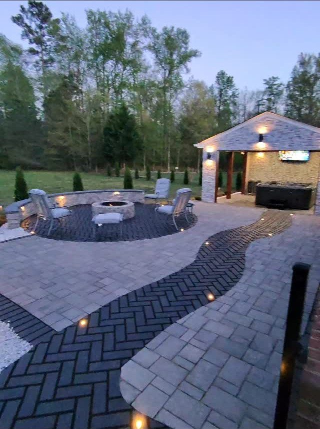16 Backyard Patio Designs for Fire Pits, Pergolas & Outdoor Kitchens 4 A stone paver patio featuring a central fire pit surrounded by outdoor seating and trees.