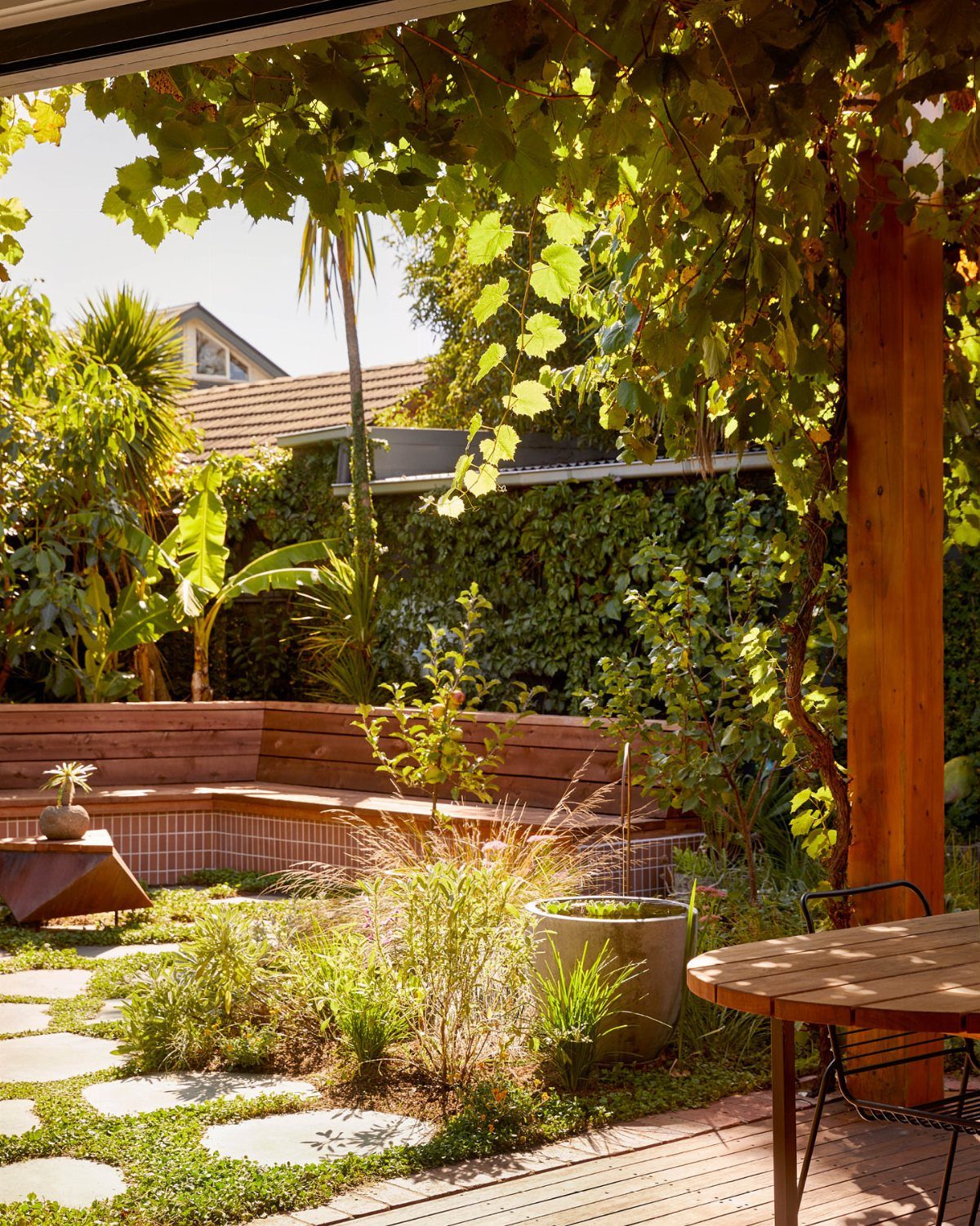 16 Backyard Patio Designs for Fire Pits, Pergolas & Outdoor Kitchens 7 Stone pavers set within green groundcover surrounded by lush garden plants and wooden patio furniture.