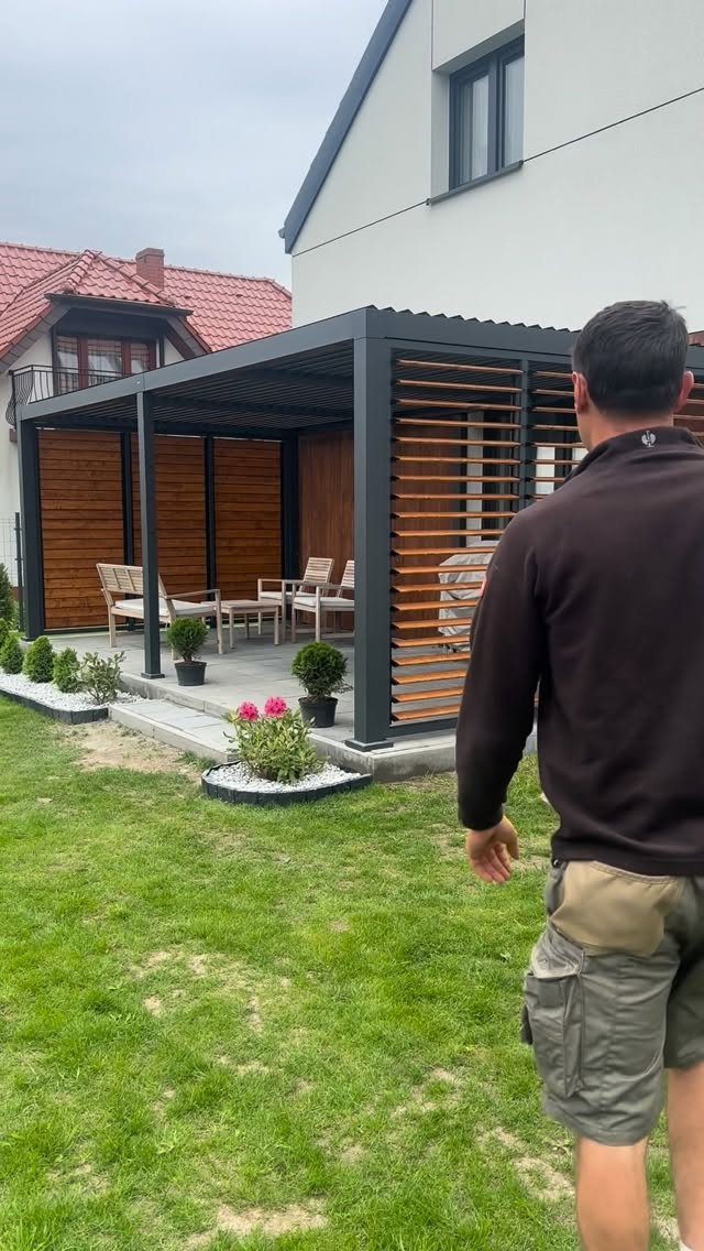 16 Backyard Patio Designs for Fire Pits, Pergolas & Outdoor Kitchens 10 A dark metal pergola with wooden slat privacy walls enclosing a patio area.