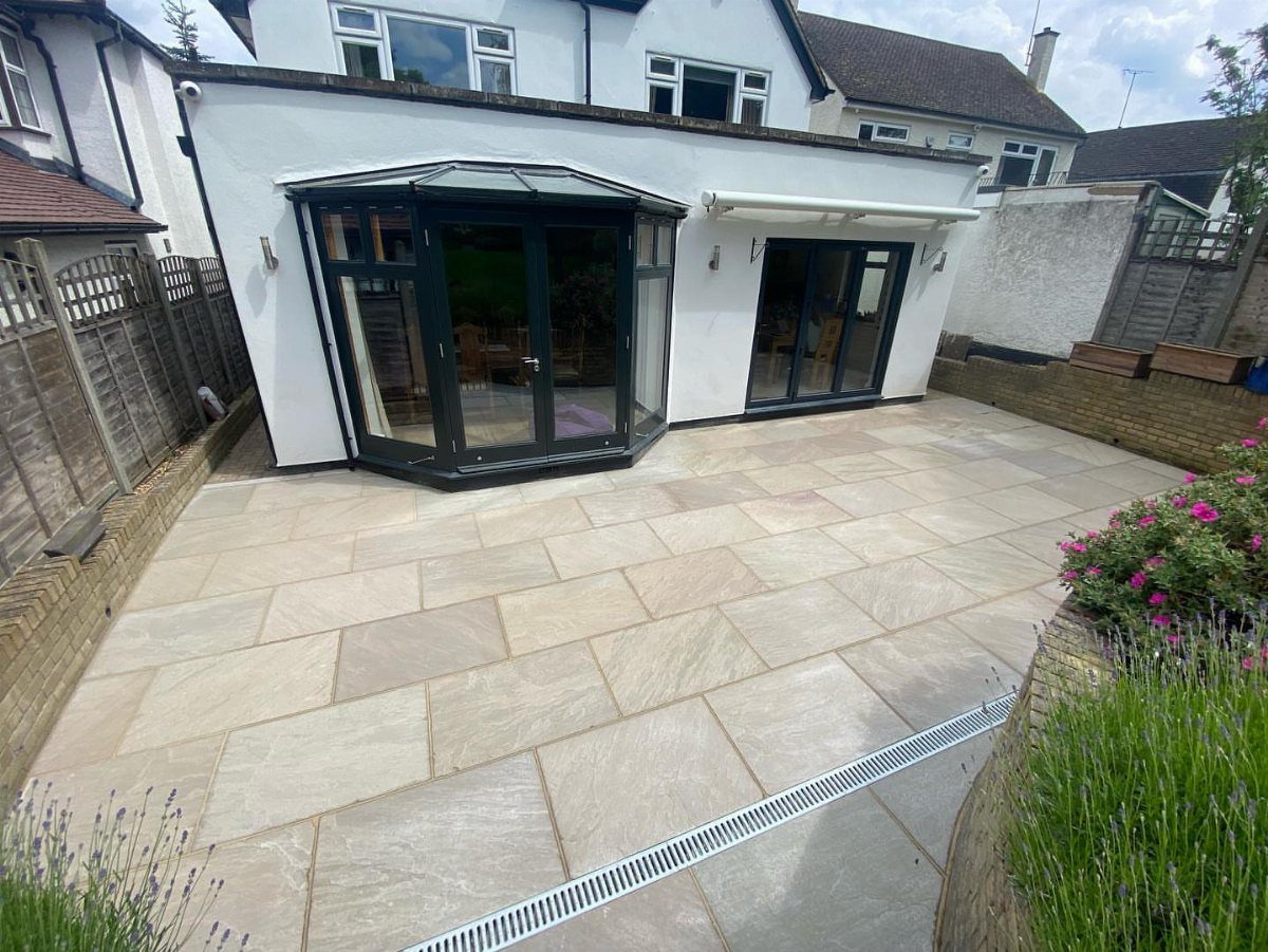 16 Backyard Patio Designs for Fire Pits, Pergolas & Outdoor Kitchens 6 Light beige sandstone pavers laid in a large patio area next to a white house.