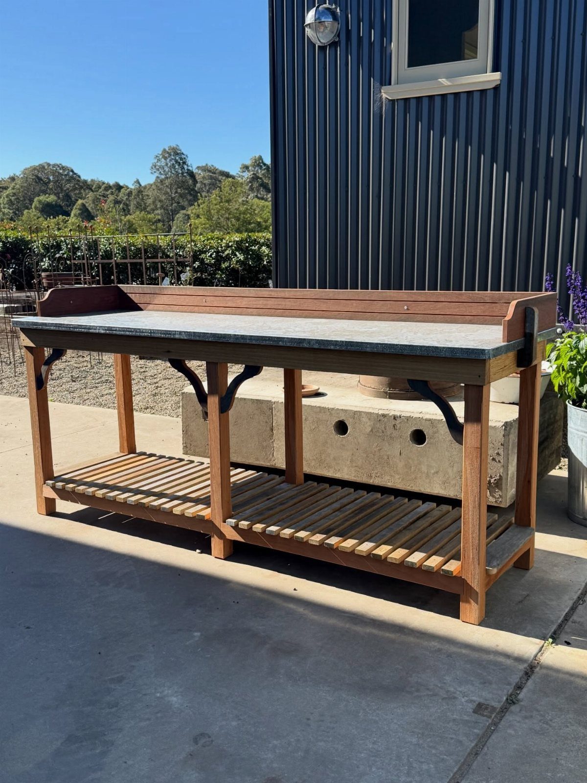 Wooden potting bench with a slatted shelf positioned on a concrete patio outdoors.