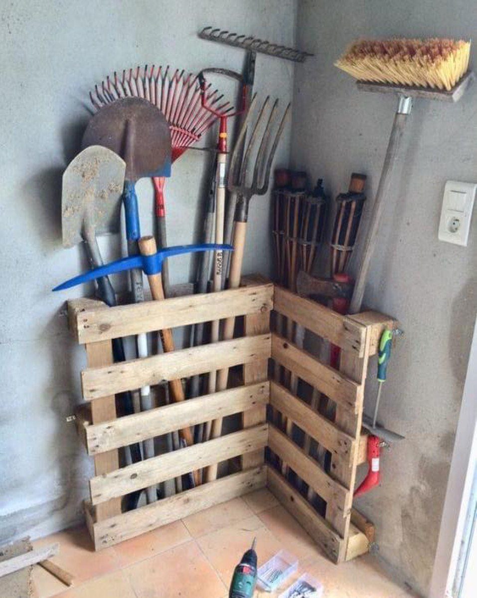 Garden tools stored upright in wooden pallets mounted in a corner against a wall.