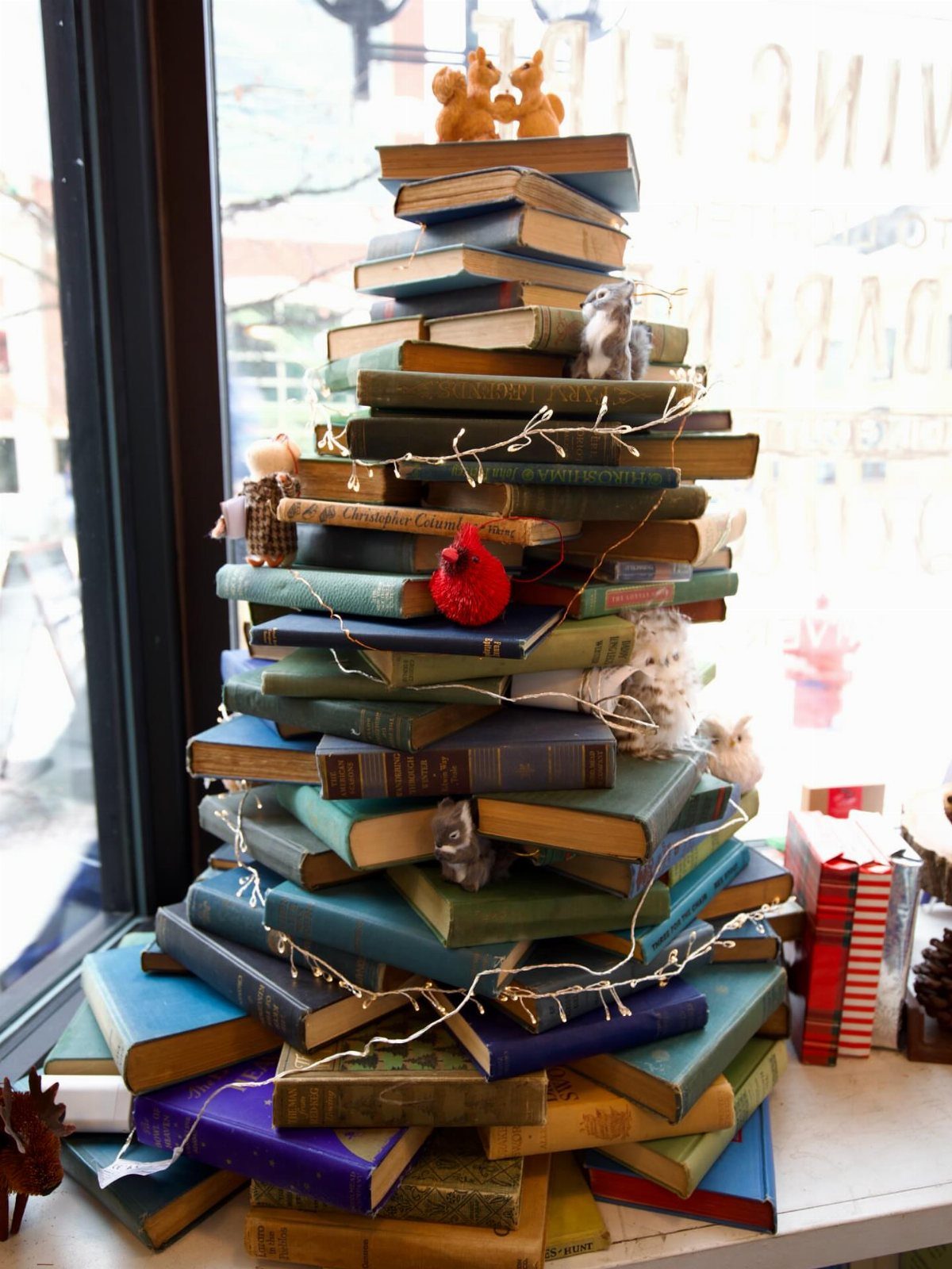 A Christmas tree constructed from a large stack of colorful vintage books decorated with lights.
