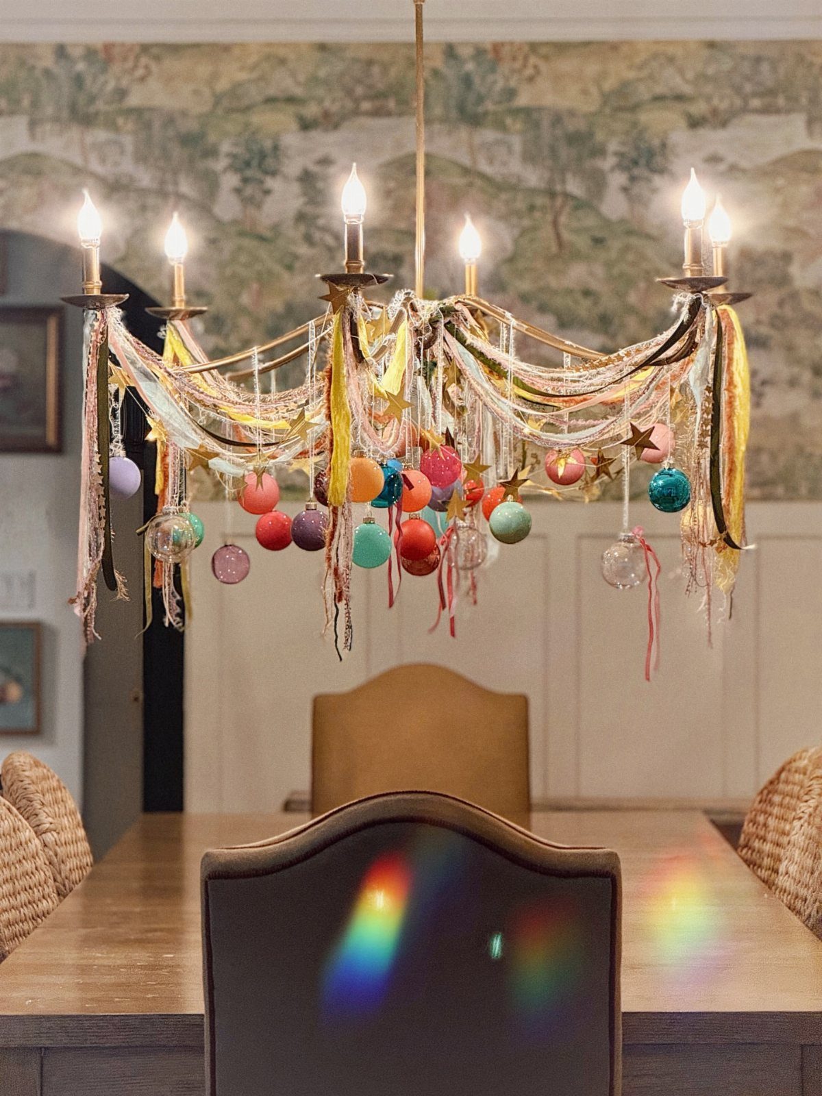 A gold chandelier decorated with colorful ribbons and hanging ornaments over a dining table.