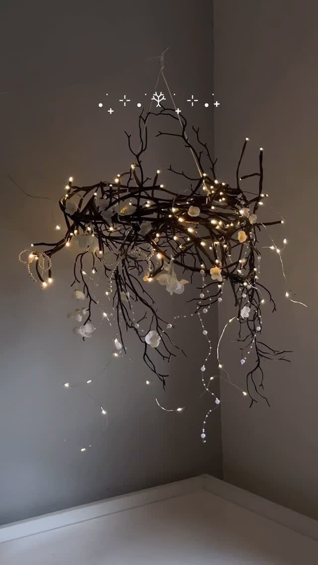 A branch chandelier decorated with white flowers and twinkling fairy lights hanging against a grey wall.