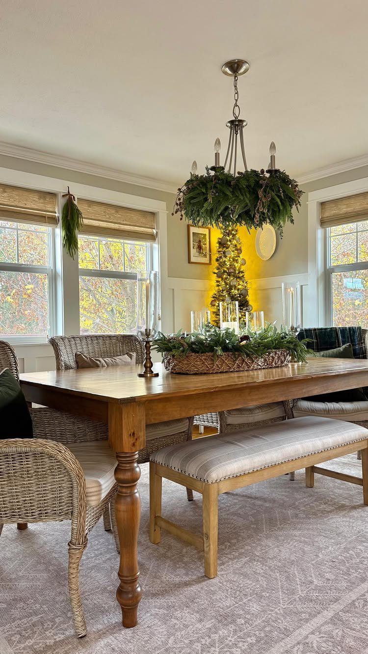 A dining room with a wooden table and a chandelier decorated with green evergreen branches.
