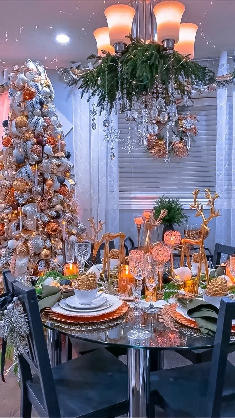 A decorated dining table with a Christmas tree and a festive evergreen chandelier.
