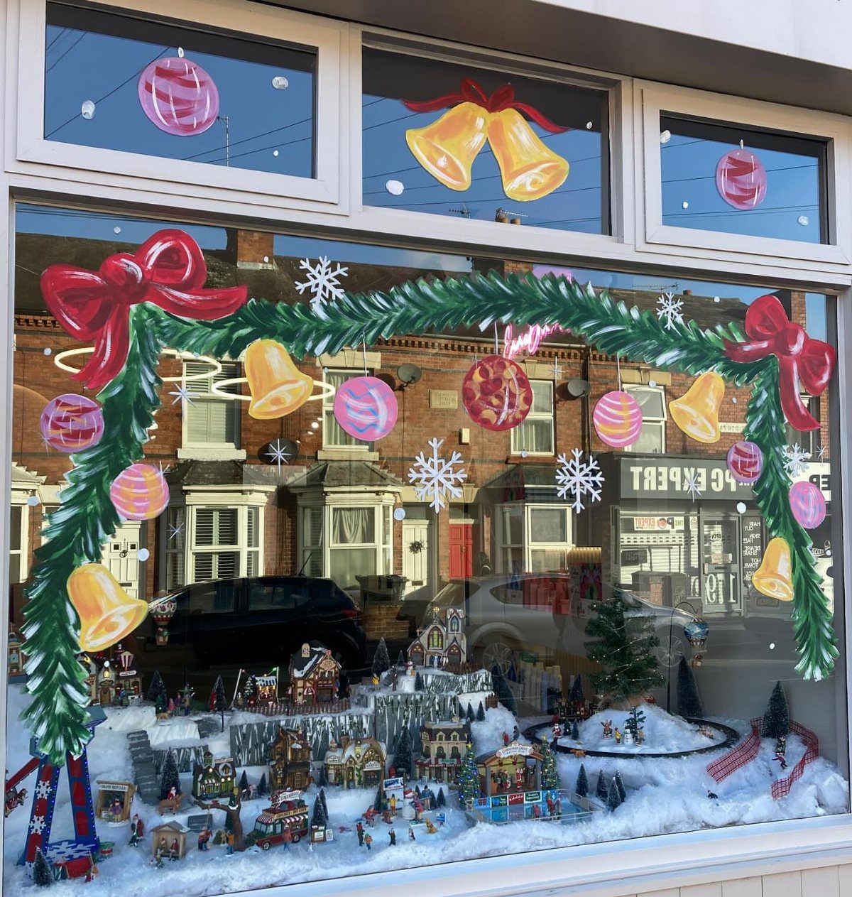 27 Christmas Display Ideas for Every Room of the Home 11 A festive storefront window display featuring a miniature Christmas village and painted holiday decorations on the glass.
