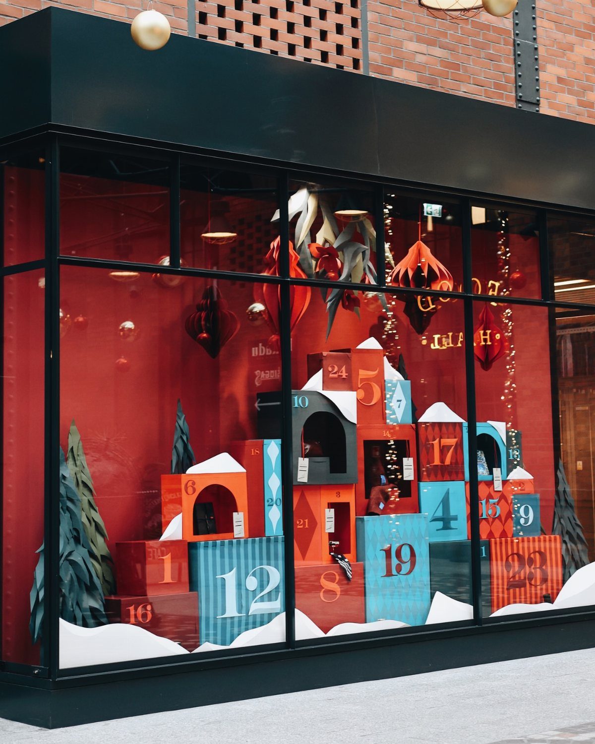 27 Christmas Display Ideas for Every Room of the Home 4 A festive red storefront window display featuring colorful numbered advent calendar boxes and miniature evergreen trees.