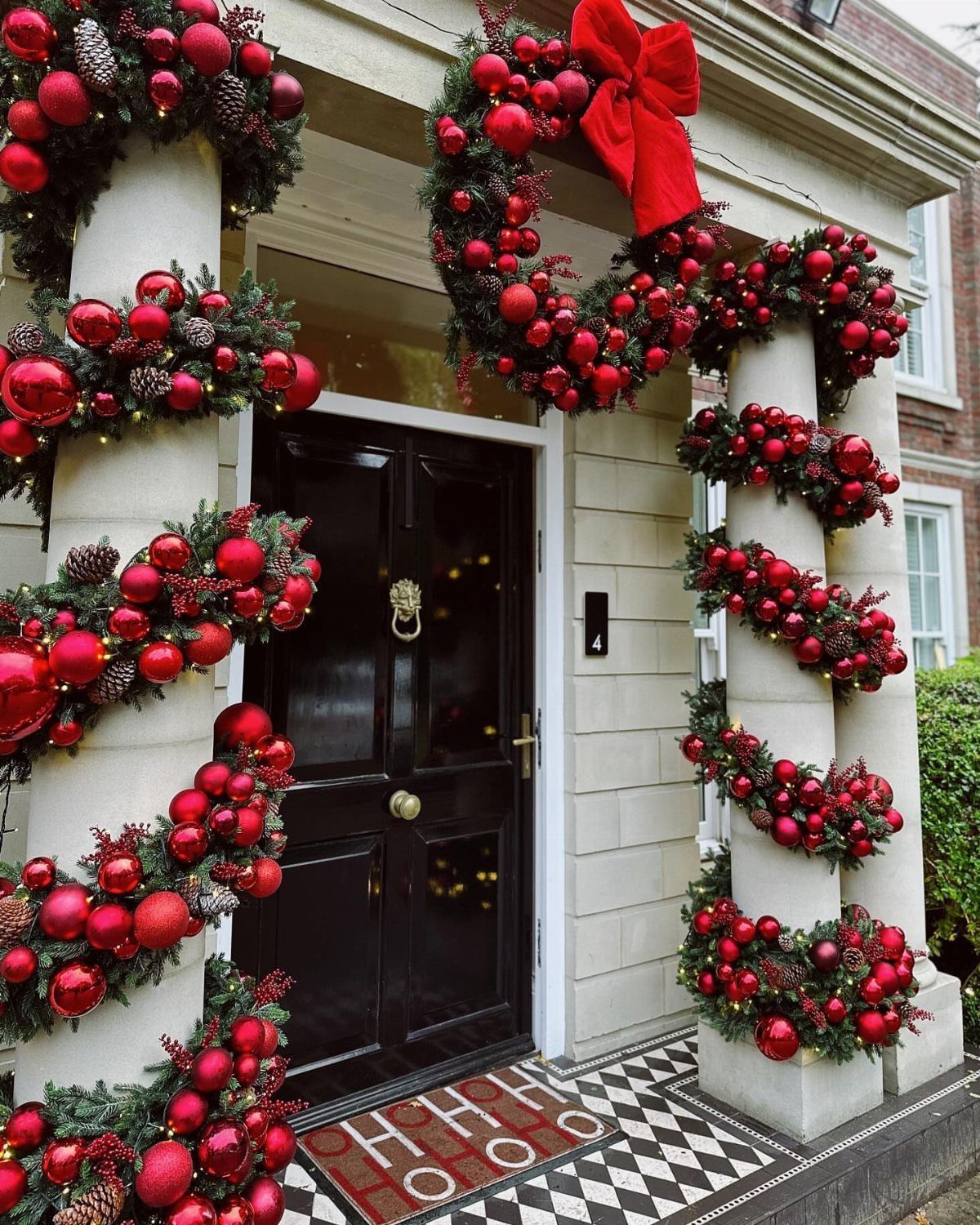 27 Christmas Display Ideas for Every Room of the Home 18 Evergreen garlands with red ornaments wrapped around white columns flanking a black front door.