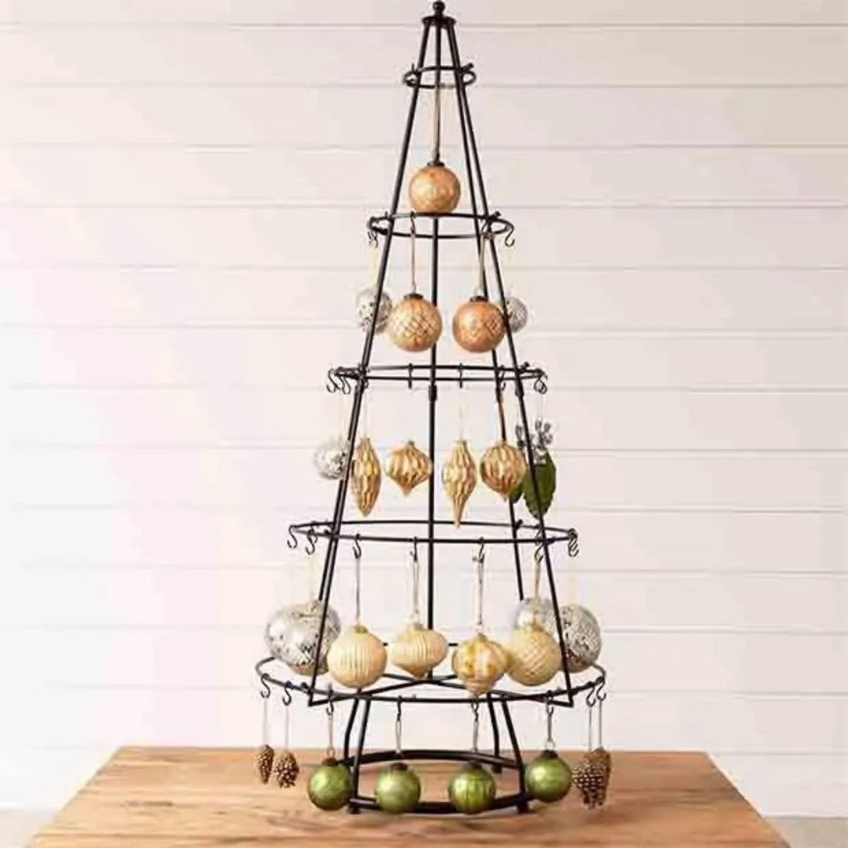 27 Christmas Display Ideas for Every Room of the Home 2 A black metal wire ornament tree stand decorated with gold and silver baubles on a wooden table.
