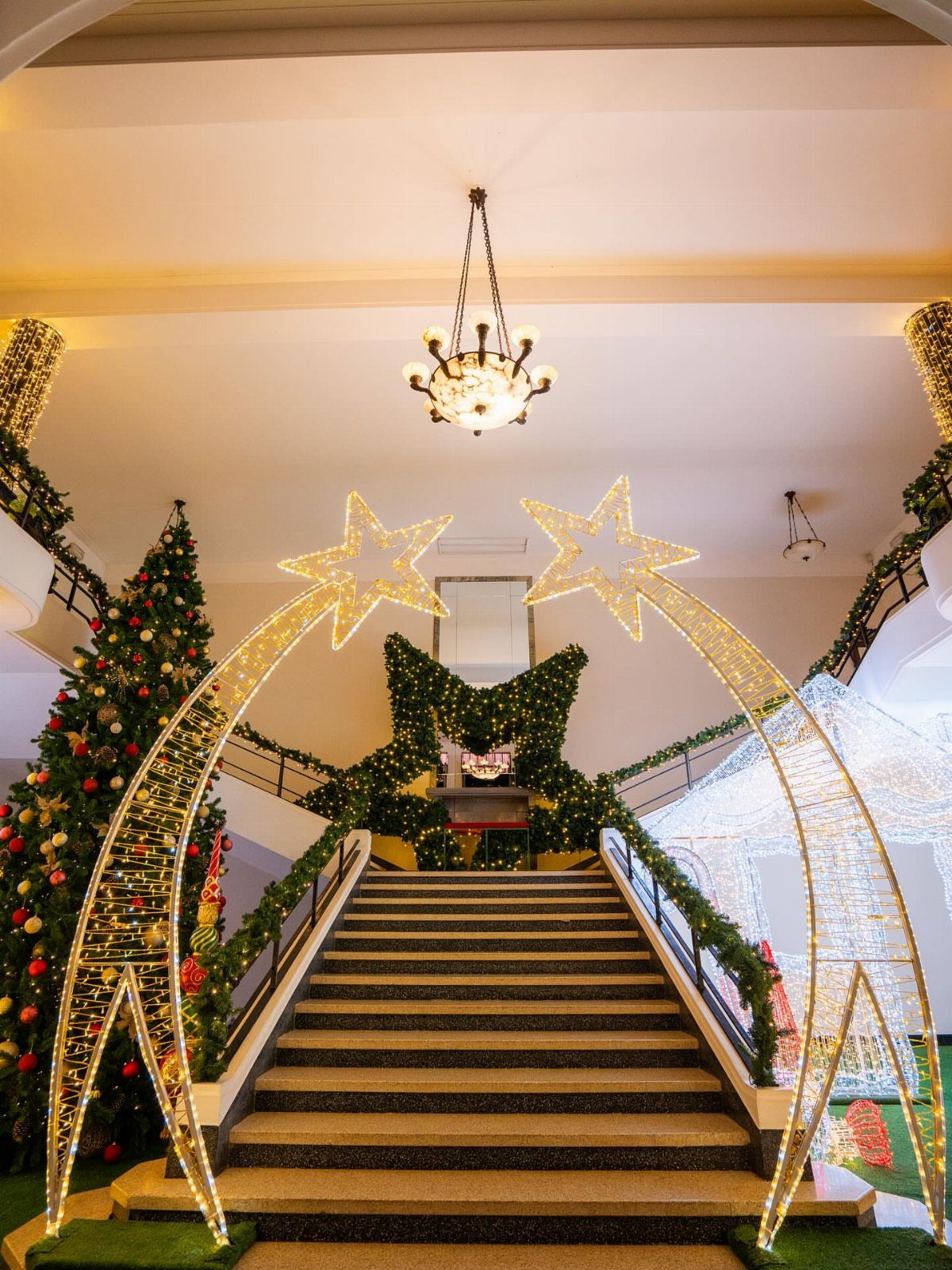 27 Christmas Display Ideas for Every Room of the Home 24 A wide staircase decorated with glowing star arches and festive Christmas garlands and trees.