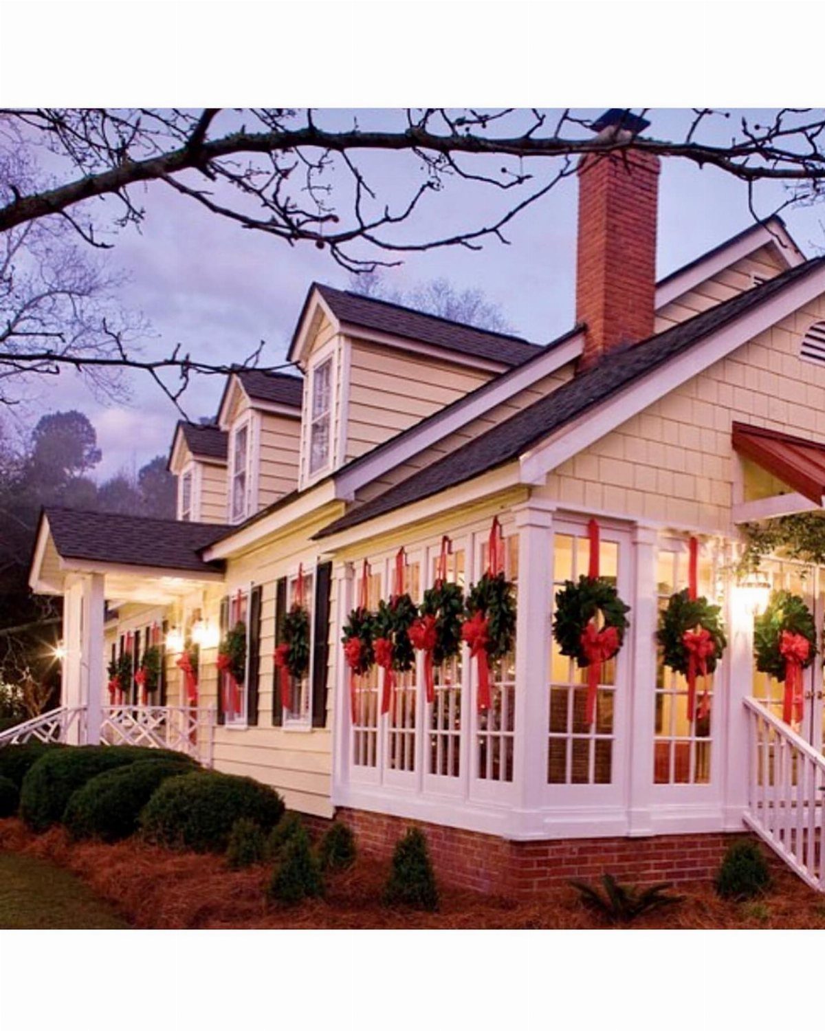 27 Christmas Display Ideas for Every Room of the Home 3 Green Christmas wreaths with red bows hanging on the white windows of a large house.