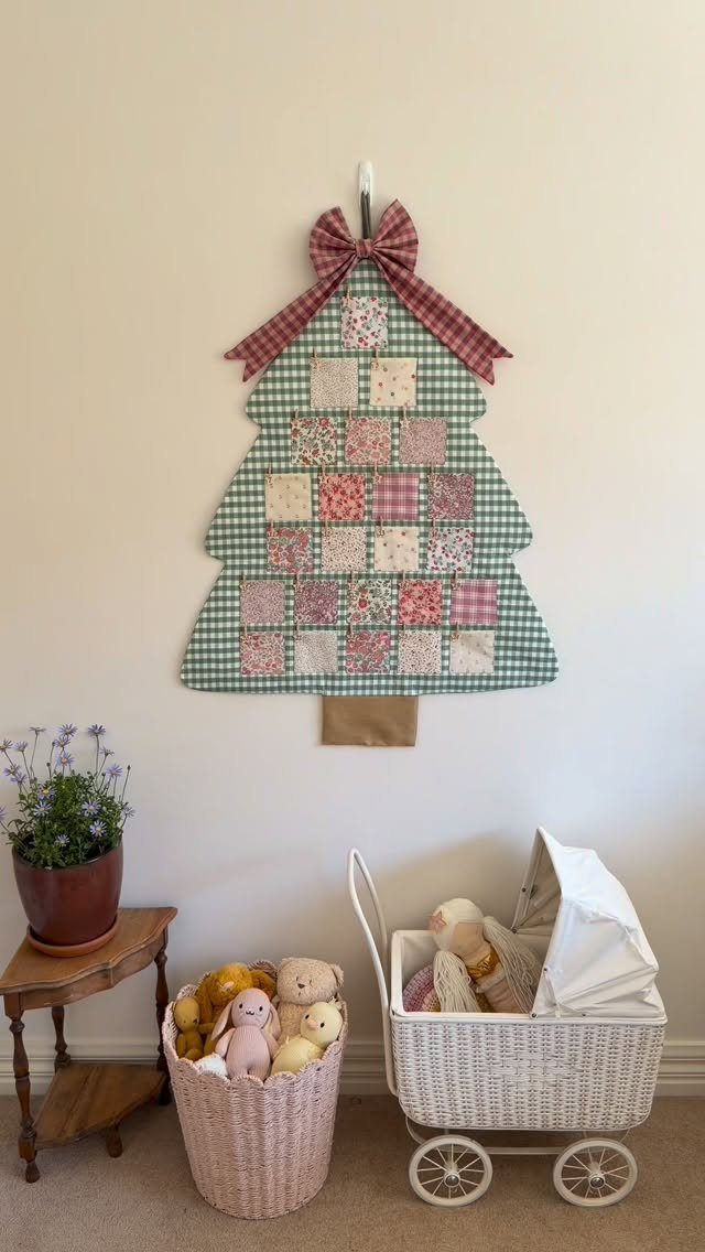 A fabric tree-shaped wall hanging with colorful patchwork squares and a large red plaid bow.
