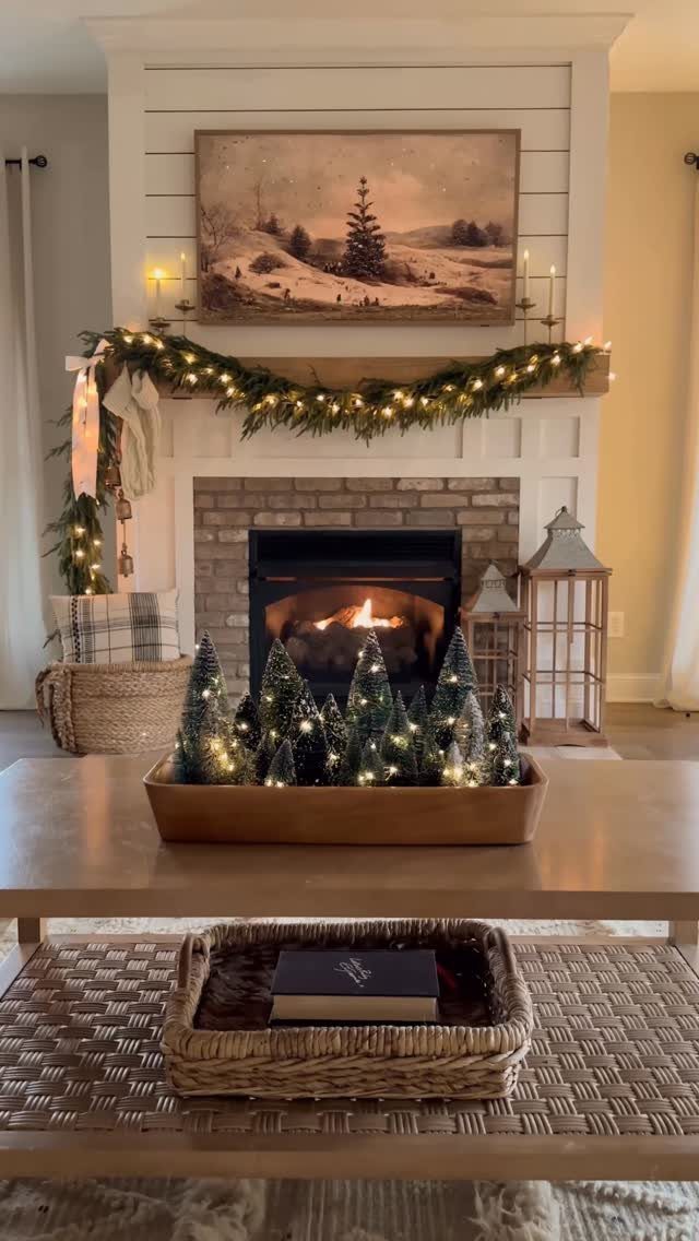 Small green bottle brush trees with lights arranged in a wooden tray on a table.