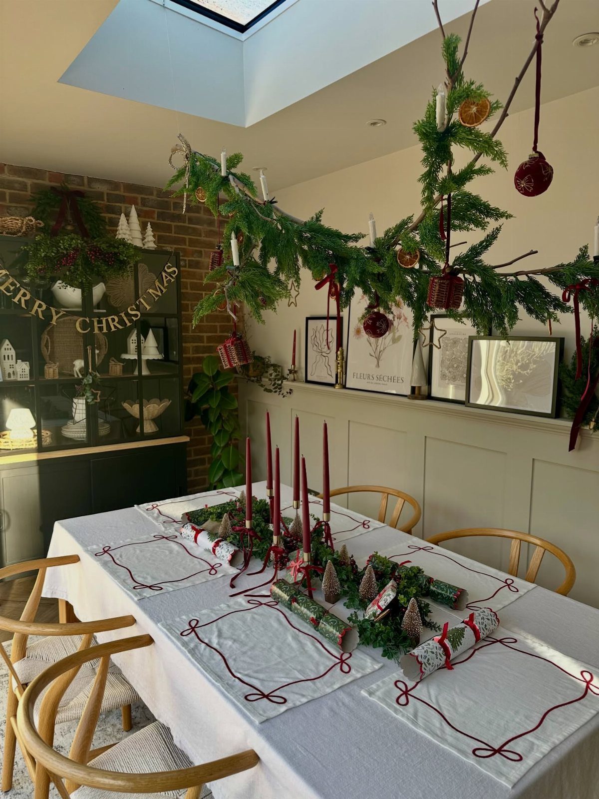 Evergreen branches decorated with ornaments and candles hanging above a festive dining table.