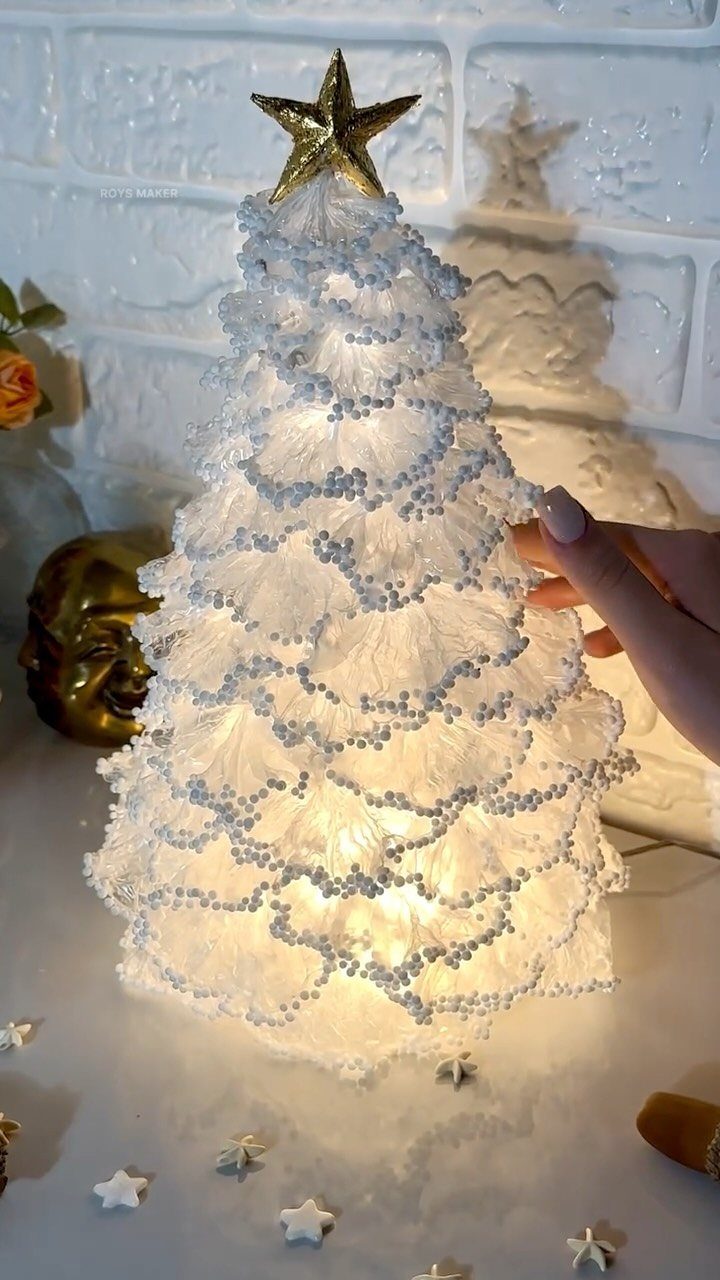 A glowing white textured decorative tree topped with a gold star on a white surface.