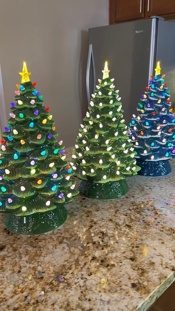 Three small glowing ceramic Christmas trees with colorful lights on a granite countertop.