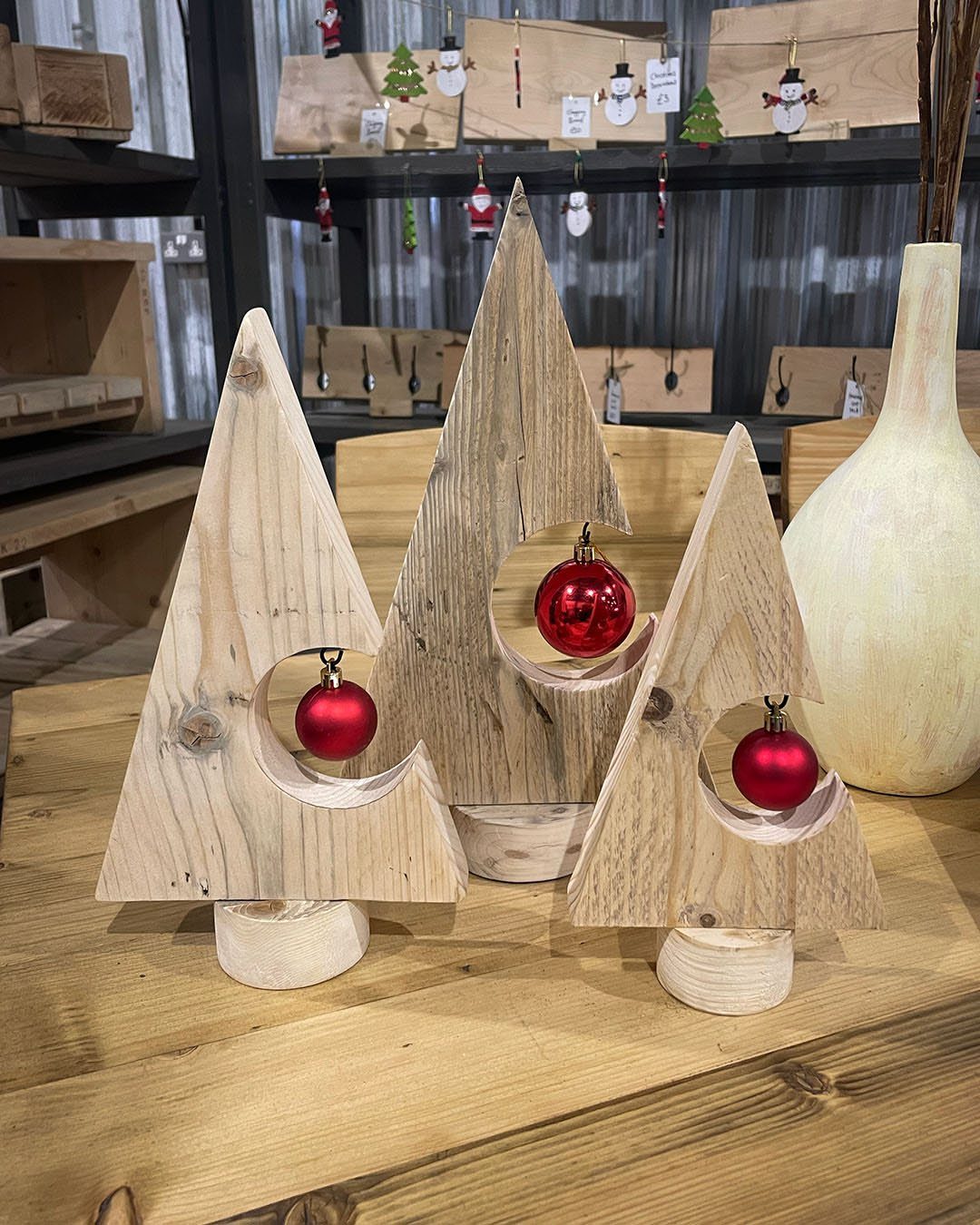 Three triangular wooden trees with red ornaments sitting on a wooden surface.