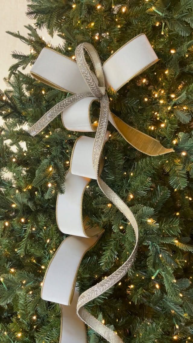 Christmas Tree Decor Ideas for 2025: 17 Fresh Styles from Coastal to Candyland 1 A large cream bow with silver glittered edges on a lit green Christmas tree.