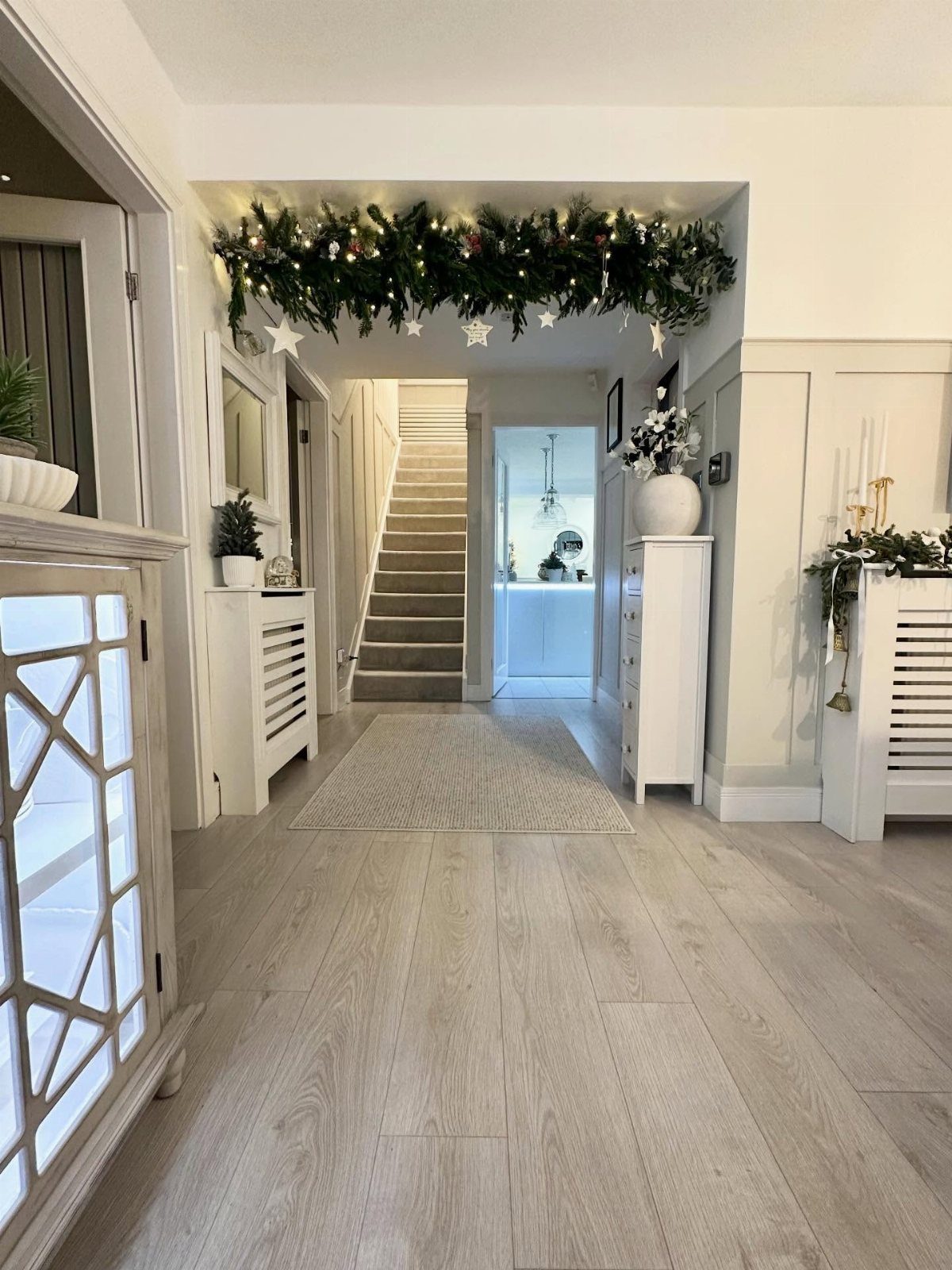 Christmas Wall Decor Ideas: 9 Ways to Dress Vertical Space 6 A bright white hallway decorated with a green garland and white star ornaments above an archway.