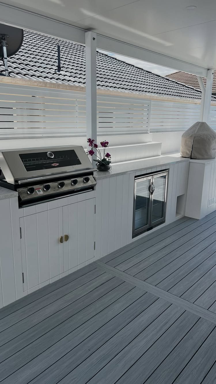 Coastal Outdoor Kitchen and 7 Ideas for Beachside Cooking Spaces 7 White outdoor kitchen with a stainless steel grill and cabinetry on a grey wooden deck.