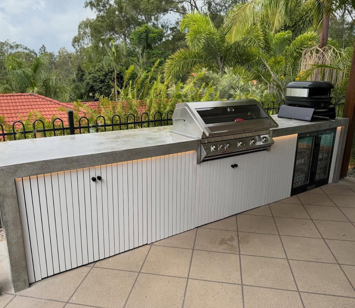 Coastal Outdoor Kitchen and 7 Ideas for Beachside Cooking Spaces 6 A modern outdoor kitchen island with a stainless steel grill and white slat cabinetry outdoors.