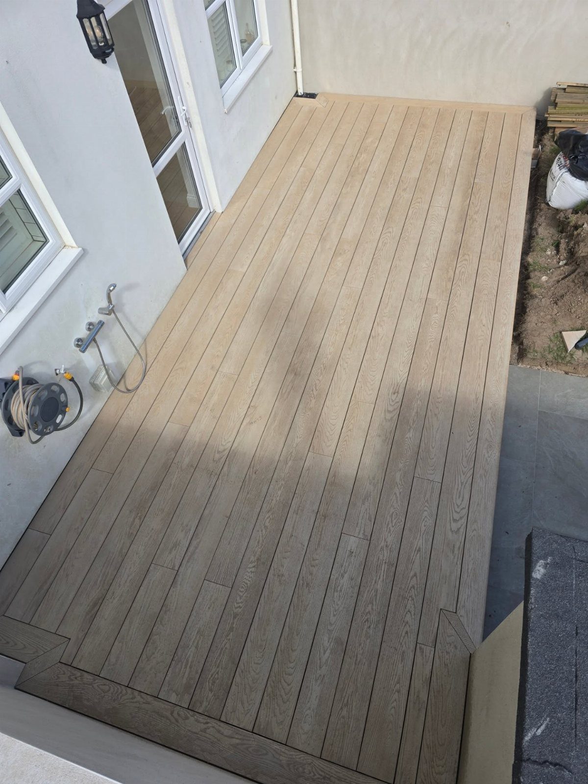 Composite Wood Deck 13 Ideas for Plans, Patterns and Colors 11 Light brown composite wood decking installed against a white house wall with glass doors.