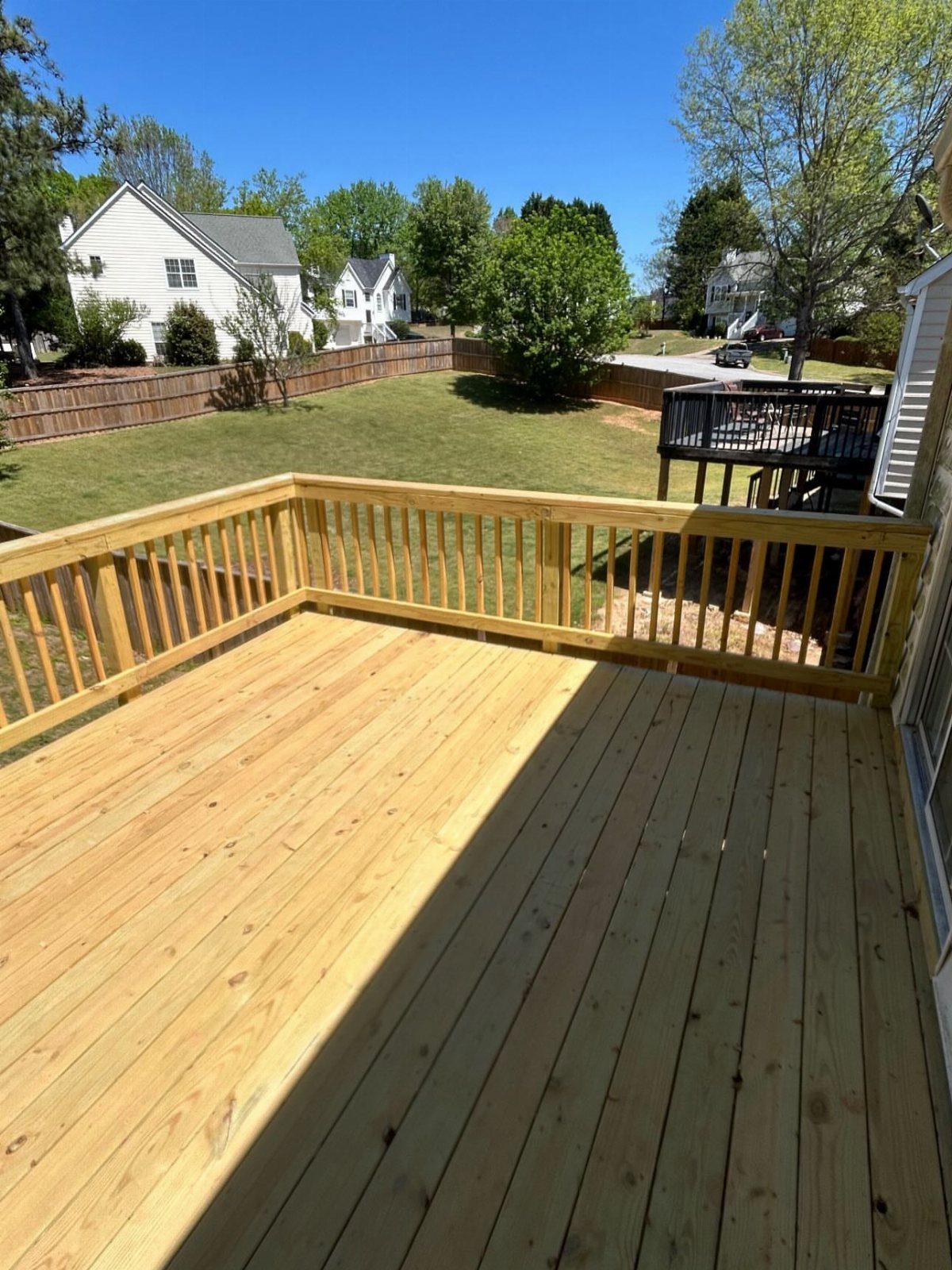 Composite Wood Deck 13 Ideas for Plans, Patterns and Colors 1 Light-colored wooden deck with railings overlooking a green backyard and suburban houses.