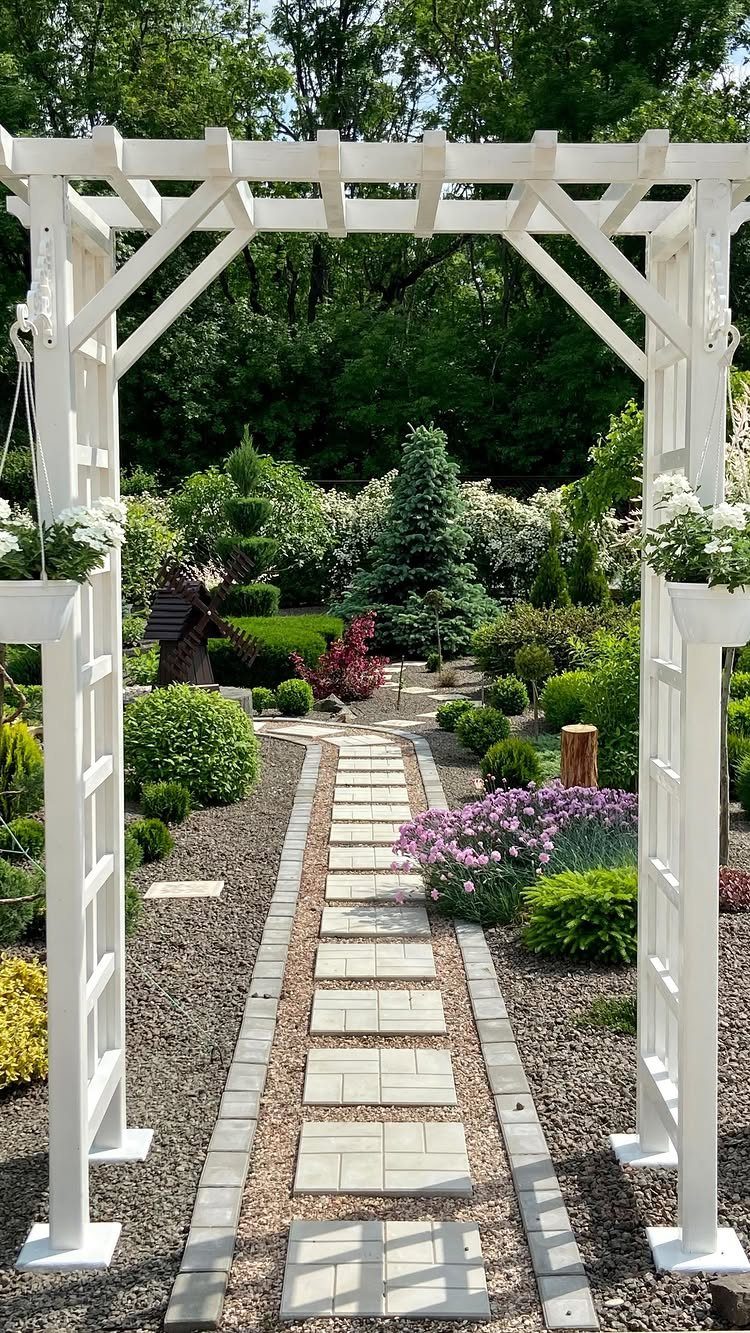 White wooden garden arch framing a stone pathway through a landscaped garden with shrubs and flowers.