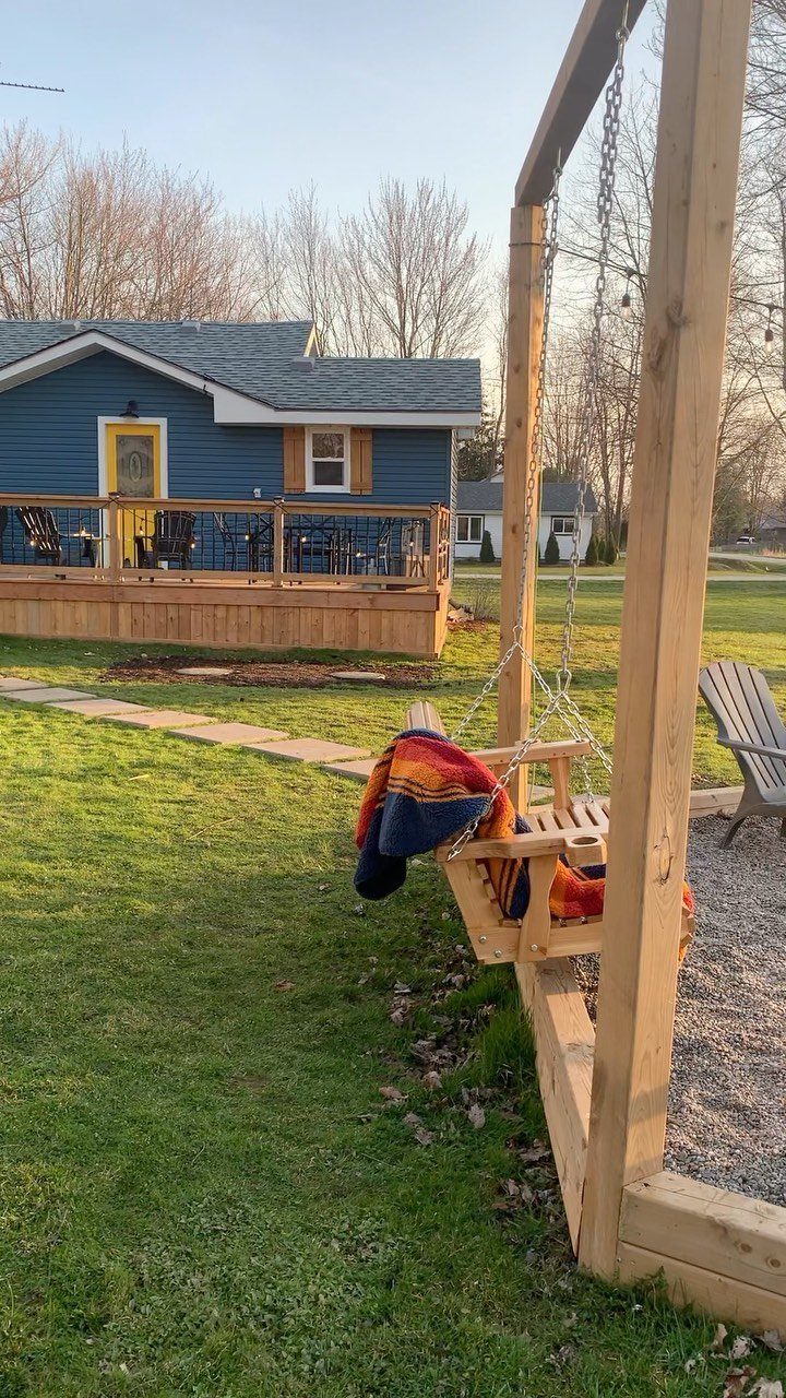 A wooden swing seat with a colorful striped blanket hangs in a grassy backyard.