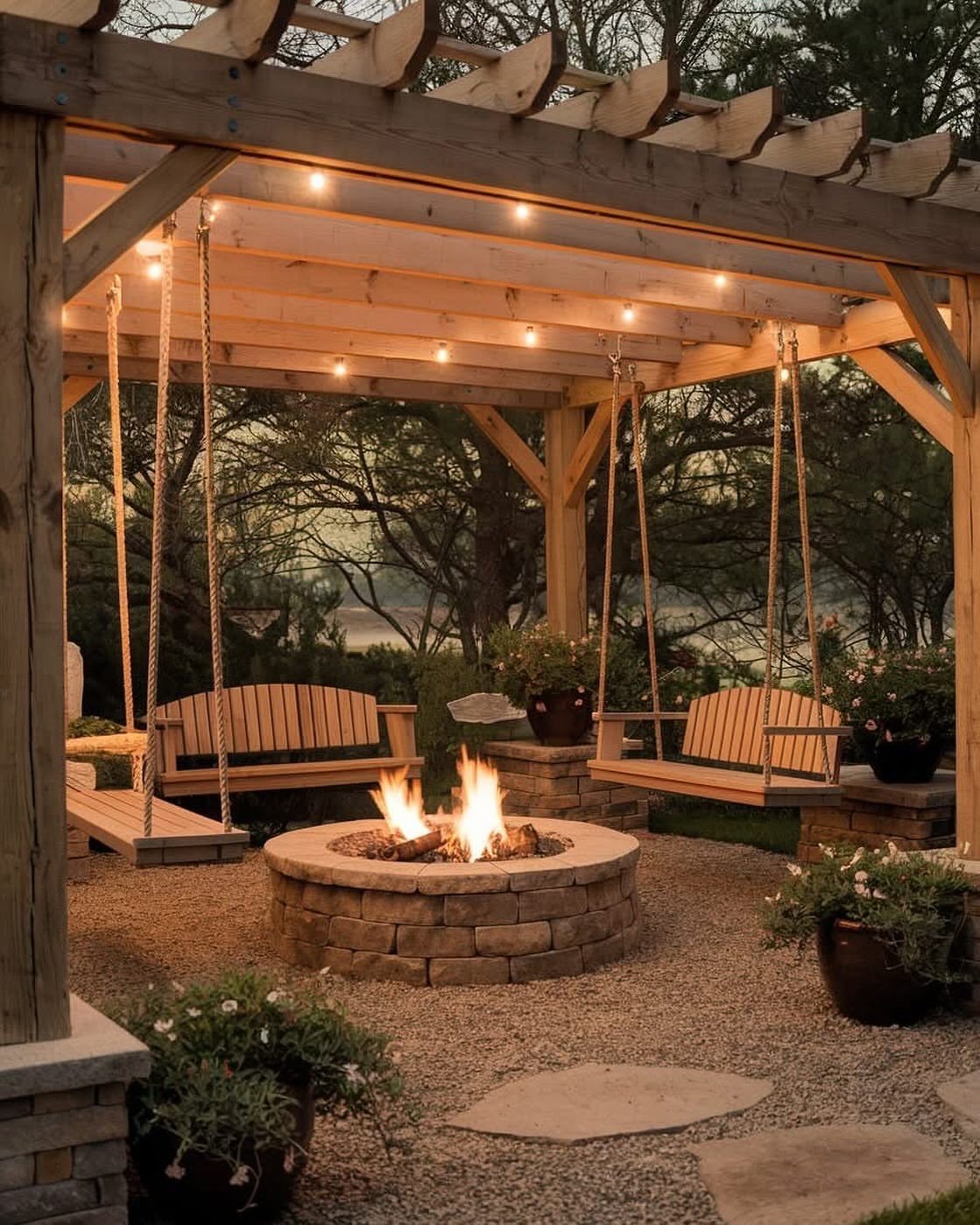 Wooden pergola with hanging swings and a stone fire pit on a gravel patio.