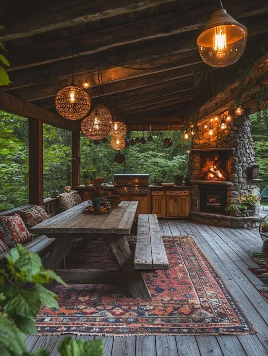 A long wooden dining table with benches sits on a patterned rug under a rustic patio roof.