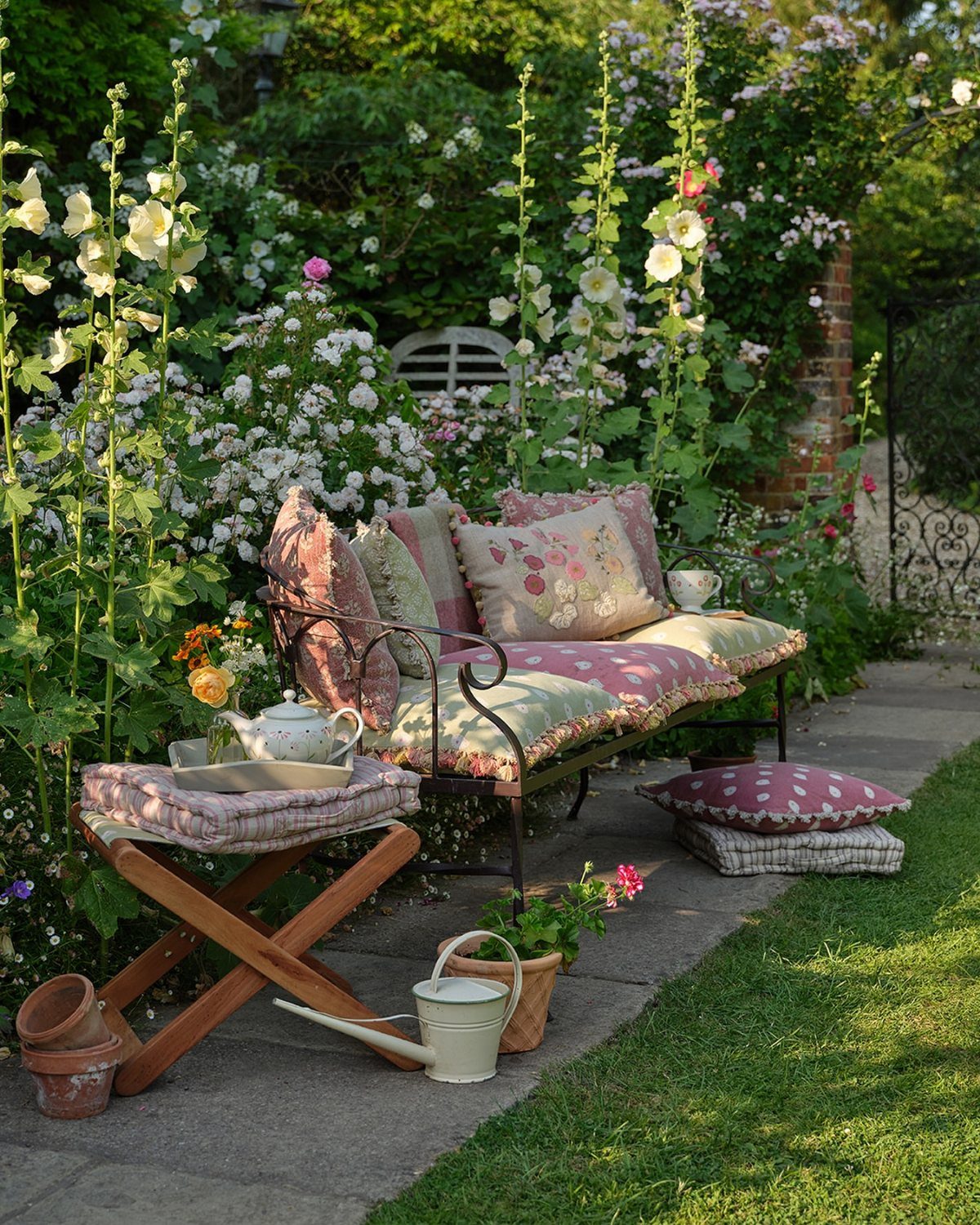 Patterned throw pillows and cushions decorating a metal garden bench in a lush flowering garden.