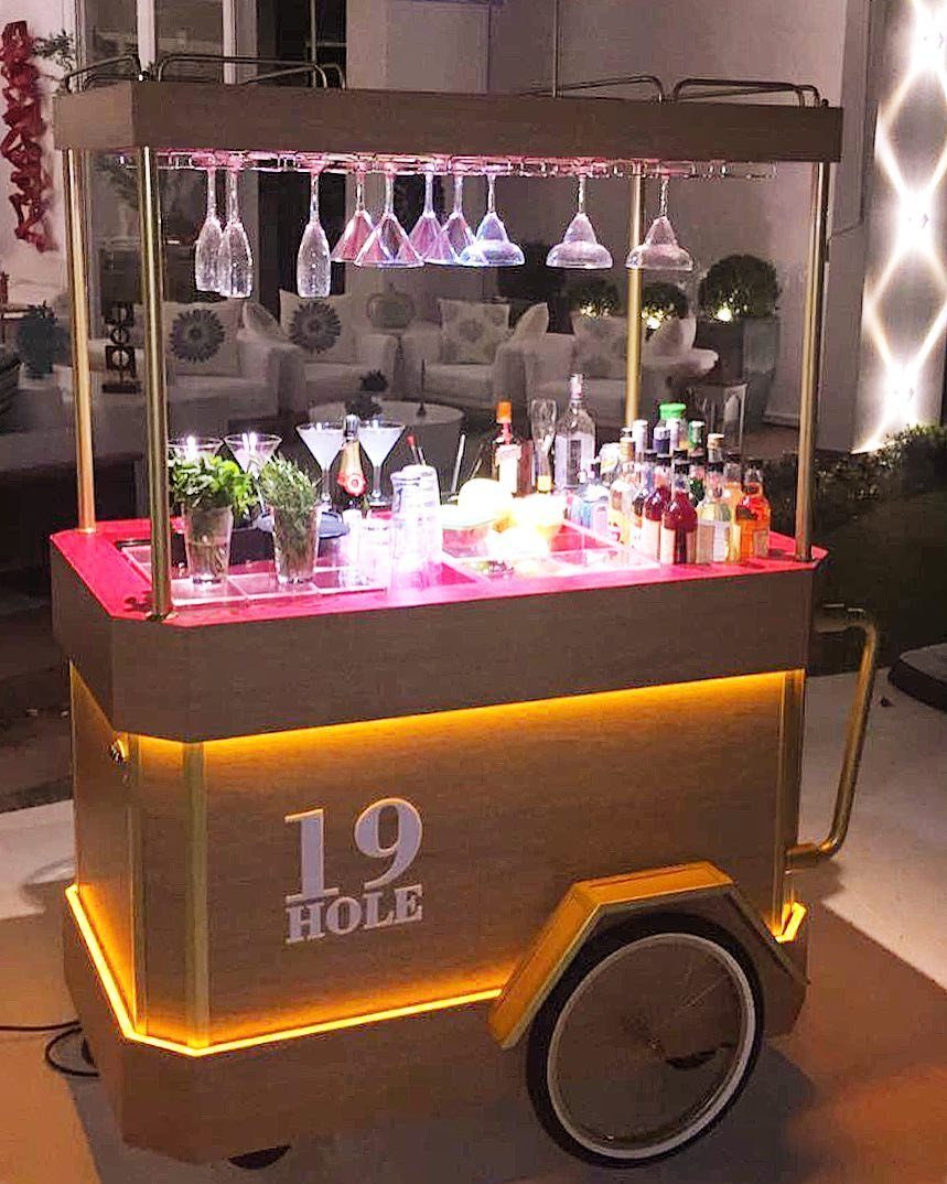 A gold mobile bar cart with glowing LED lights, liquor bottles, and hanging glassware.