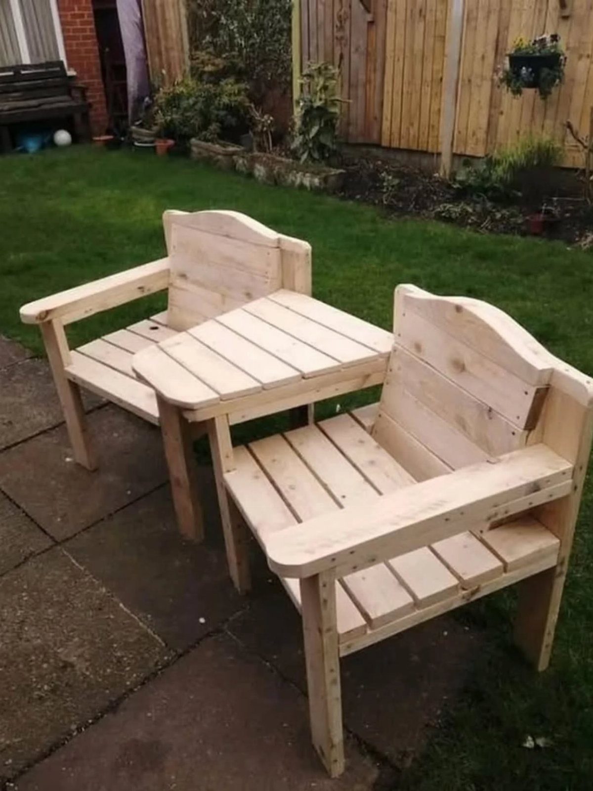 Two light wood armchairs with a small matching slatted table on a stone patio.