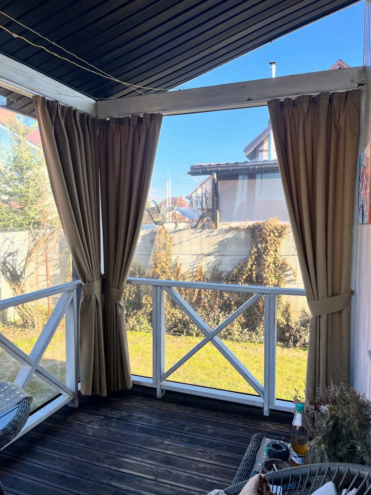 Tan outdoor curtains tied back on a white wooden deck railing under a dark pergola.